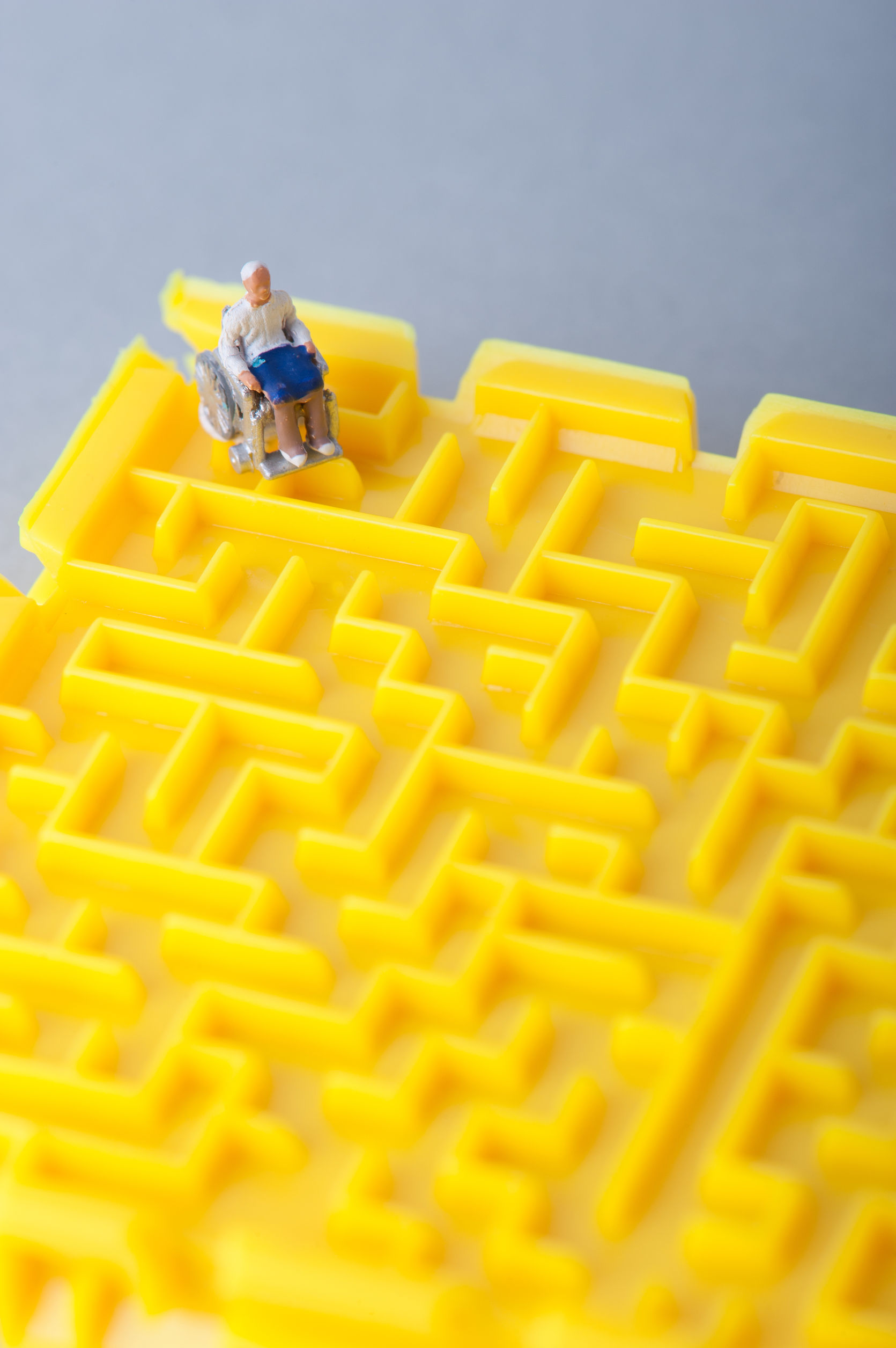 Miniature human in wheelchair and trapped in a yellow maze