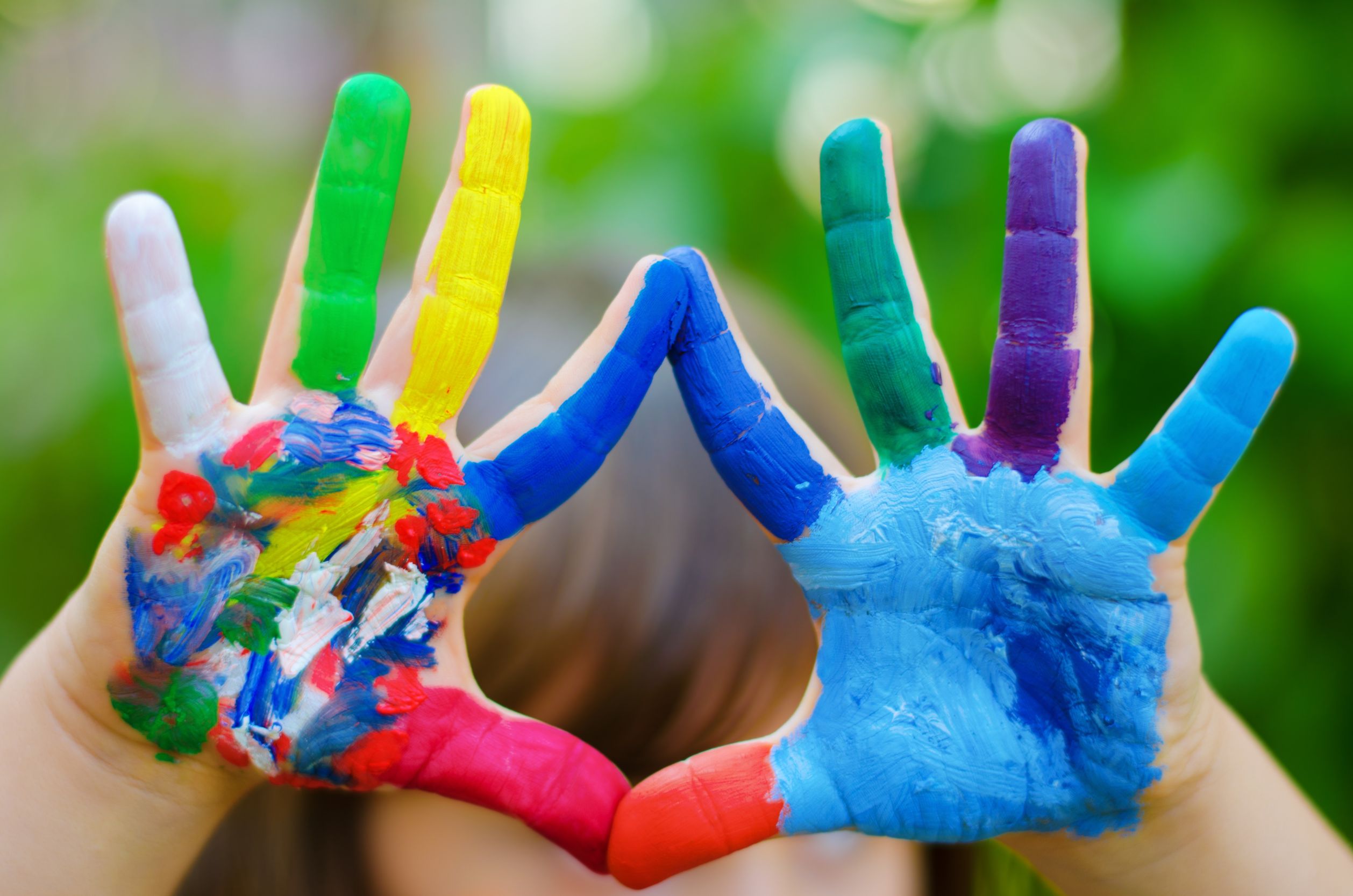 Photo of a child’s hands covered in paint of different colours
