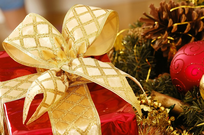 A festive image showing a present wrapped in red and tied with a gold ribbon