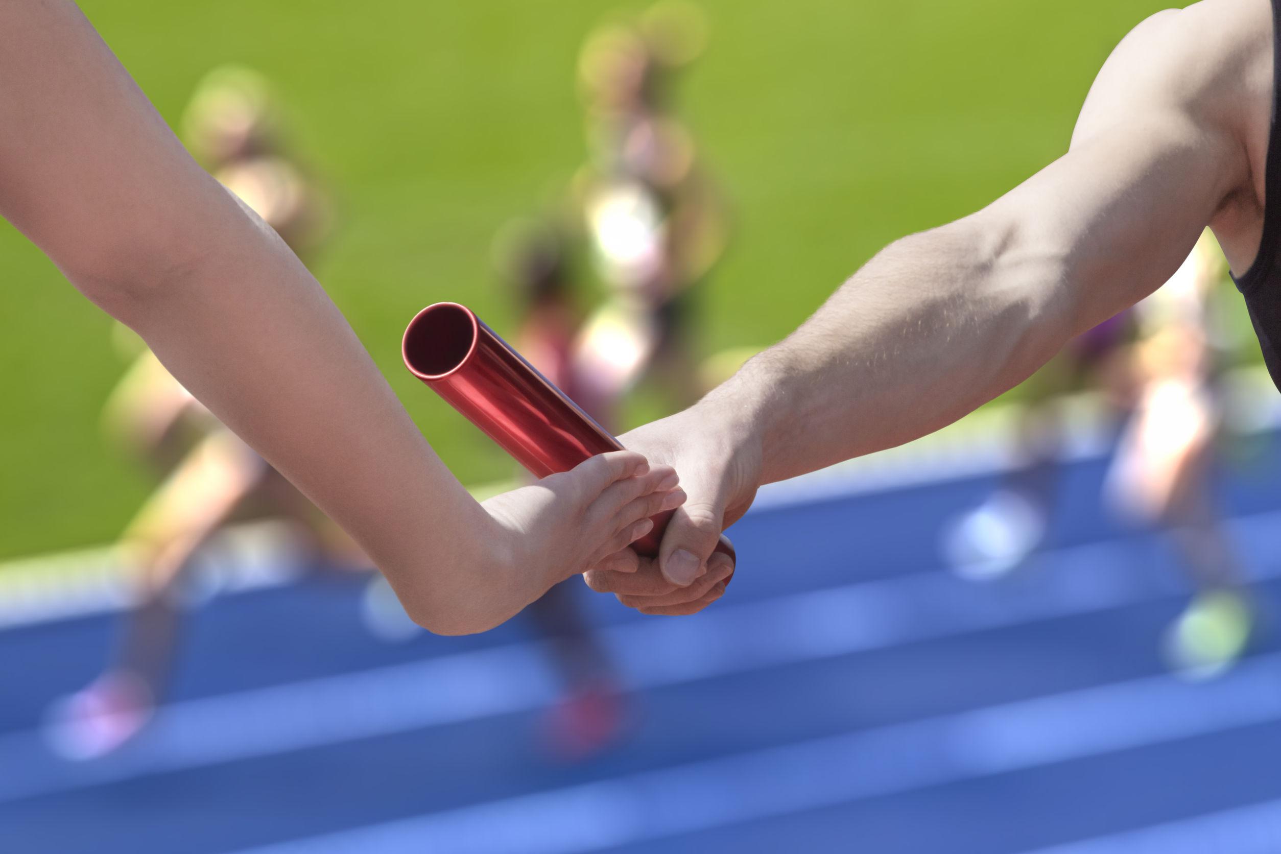 Close-up of the hand of an athelete passing the baton to another athlete during a relay race