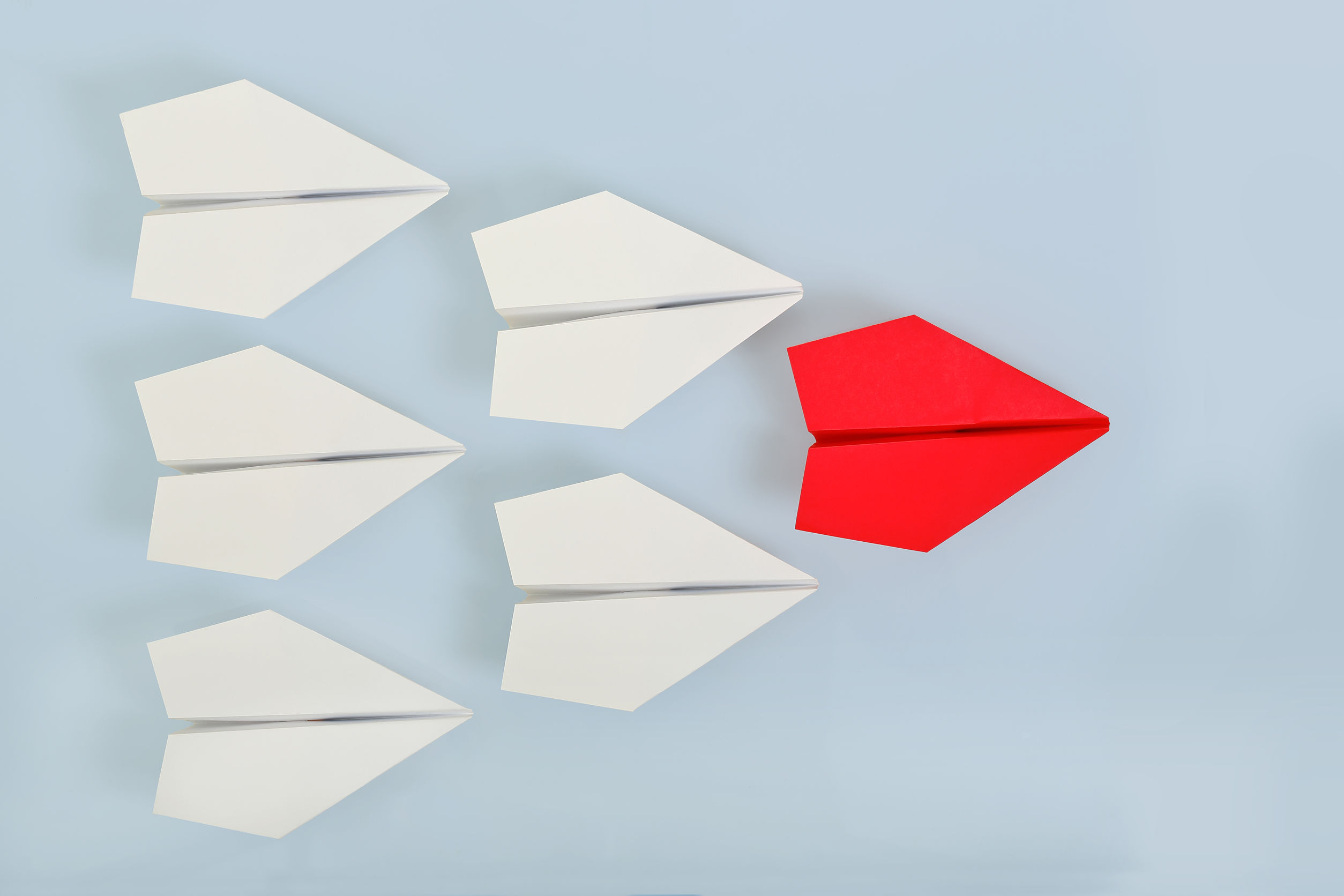 A red origami plane leading several white origami planes