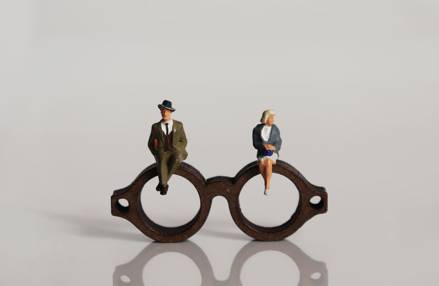 Photo of a miniature man and a miniature woman sitting on a pair of glasses