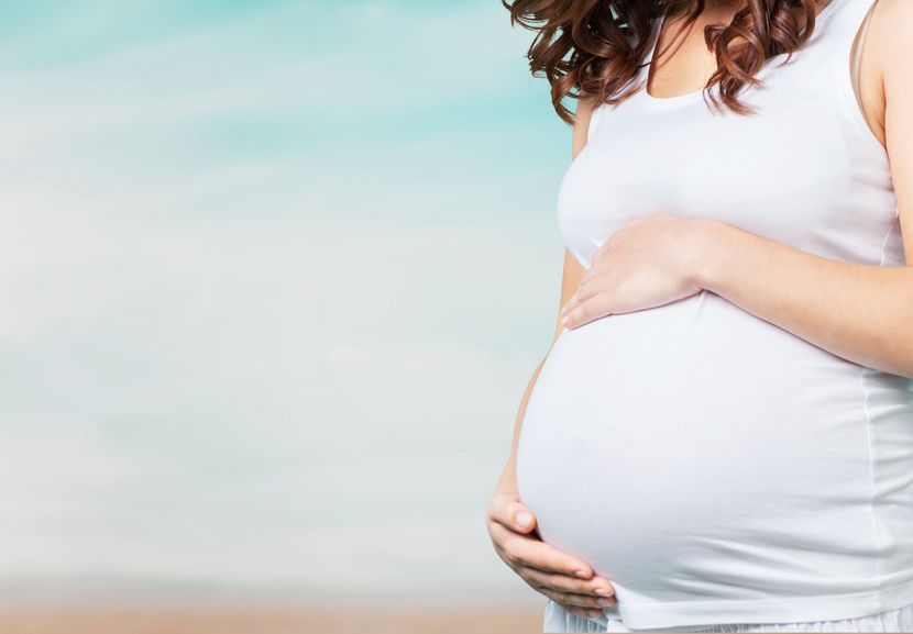 Photo of a pregnant woman dressed in white, holding her belly