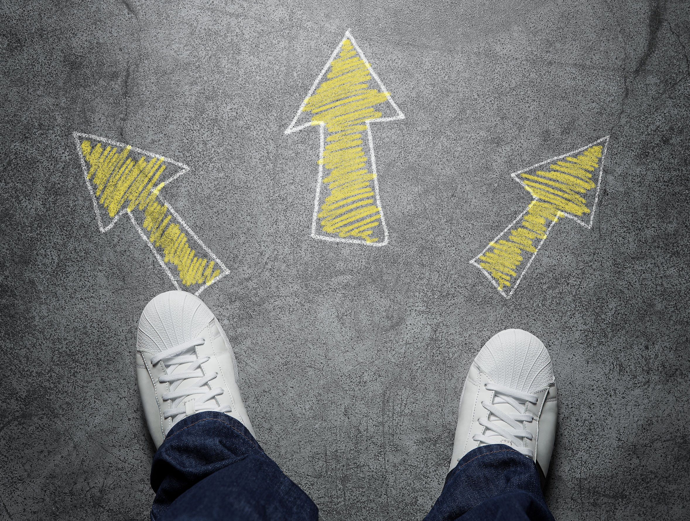 Photo of a person looking down at her/his feet, with three yellow arrows drawn on the path in front.