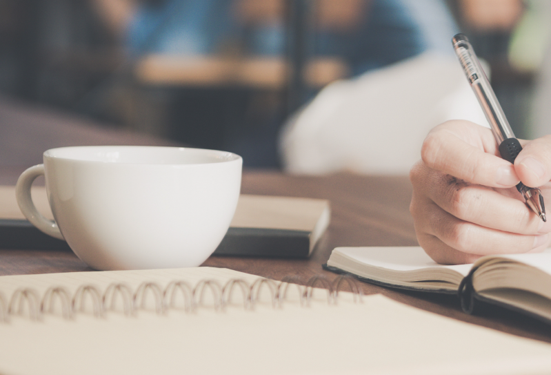 插圖：咖啡杯，旁邊是一本筆記簿，有人在上面寫字。