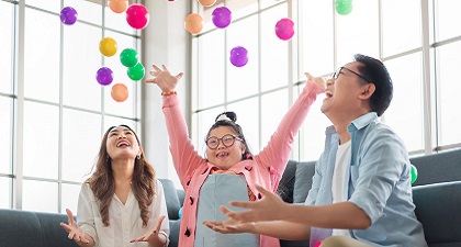 Parents and a child with down syndrome are sitting on a sofa and throwing colour balls into the air