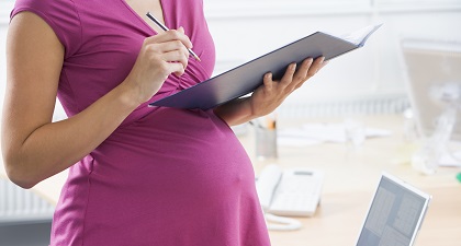 A pregnant woman is holding a file and a pen in an office